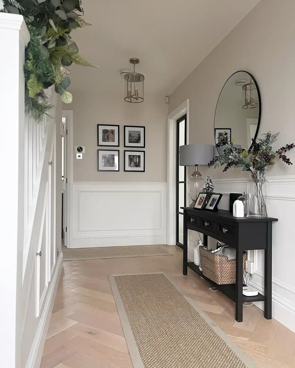 Neutral hallway with black console table, arched mirror, gallery frames, woven runner, and greenery