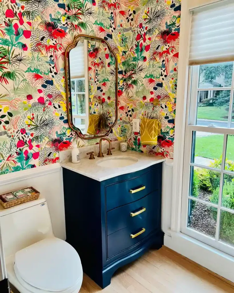Colorful tropical wallpaper surrounds a navy vanity with brass hardware and a curved mirror in a bright powder room.
