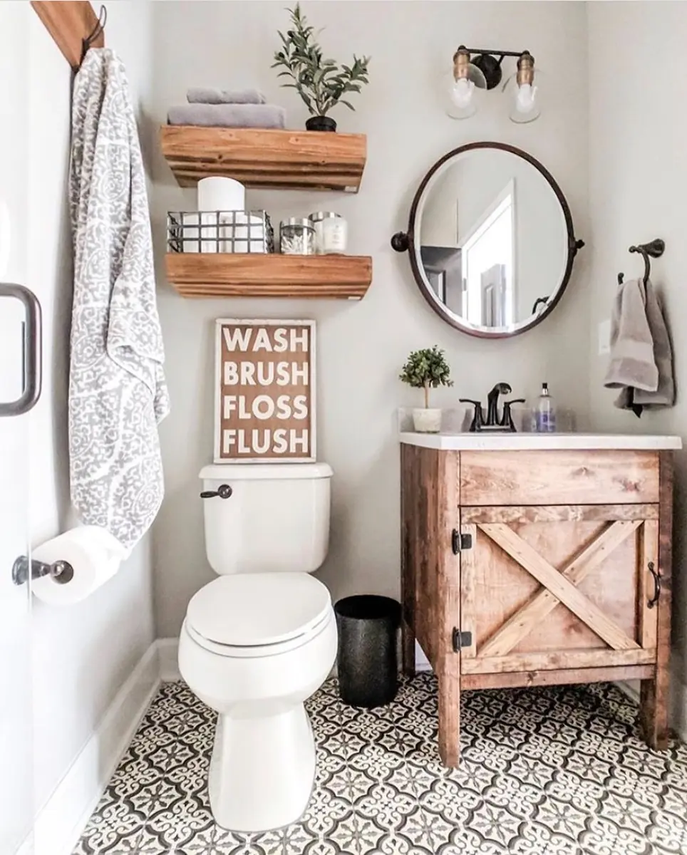 Small rustic bathroom with wooden wall shelves, a round mirror, barn-style vanity, and patterned tile floor.