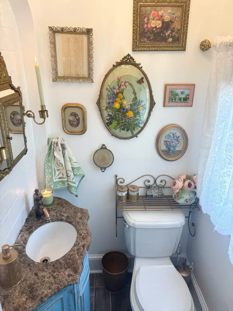 Vintage bathroom gallery wall with ornate gold frames, floral needlework, and small framed artwork above the toilet.