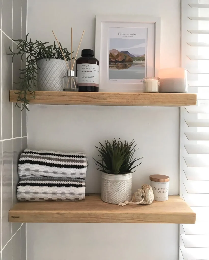 Warm wood bathroom shelves with folded towels, greenery, framed art, candles, and a reed diffuser.