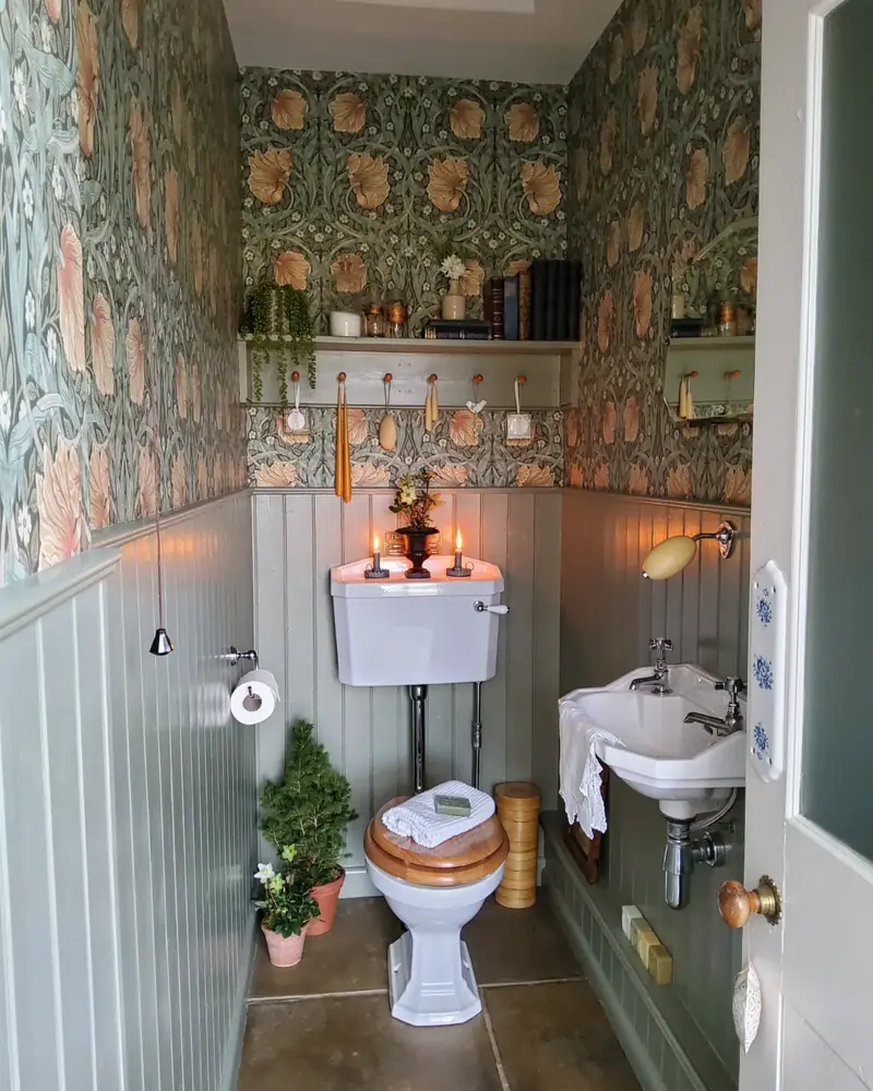 Narrow vintage bathroom with green floral wallpaper, gray paneling, a compact sink, and a white toilet.