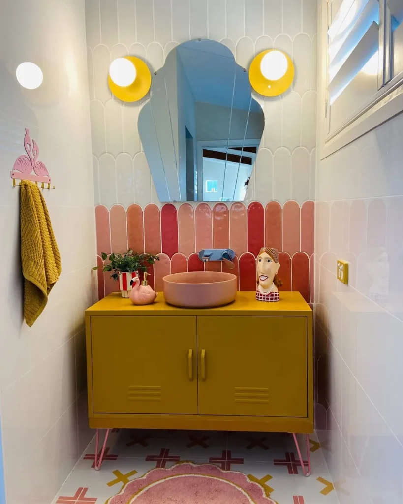 Colorful bathroom counter with a mustard vanity, blush pink sink, pink tile, small plant, and playful decorative accessories.