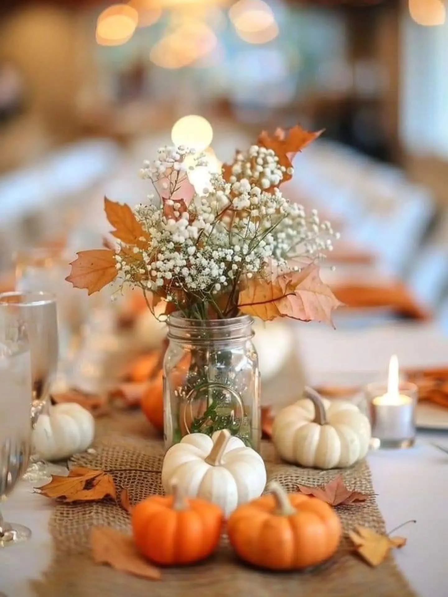 Baby’s breath and orange leaves in a mason jar centerpiece surrounded by mini pumpkins and candlelight