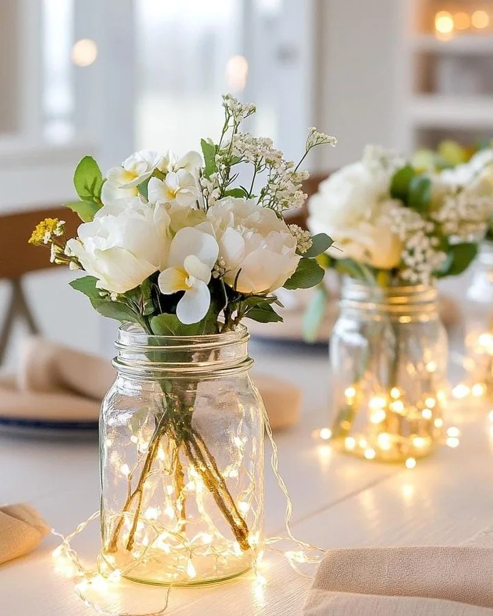 White flowers arranged in a clear mason jar glowing with warm fairy lights