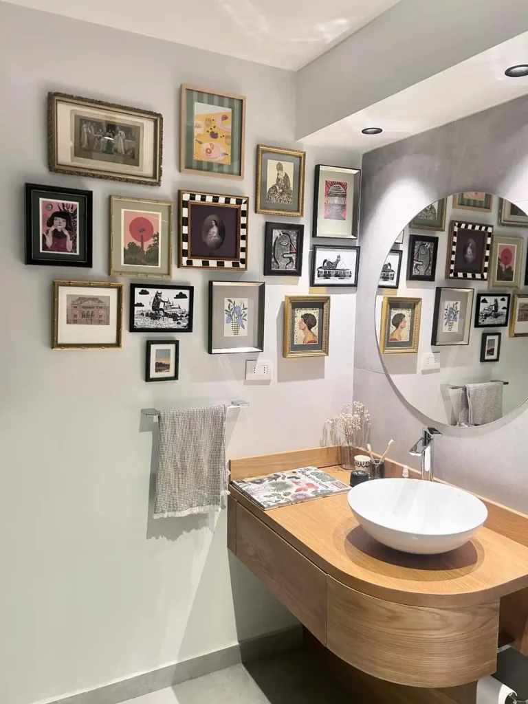 Modern bathroom gallery wall with mixed black, gold, and wood frames arranged beside a large round mirror.