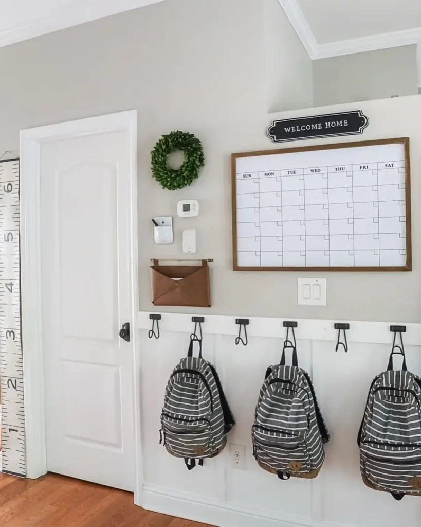 Entryway command center with backpack hooks, family calendar, wall pocket, and white board-and-batten wall.