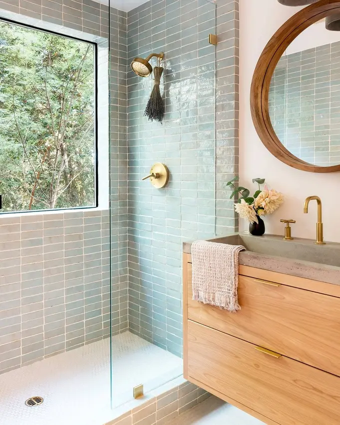 Small bathroom with a frameless glass shower, pale blue tiles, a floating wood vanity, and brass fixtures.