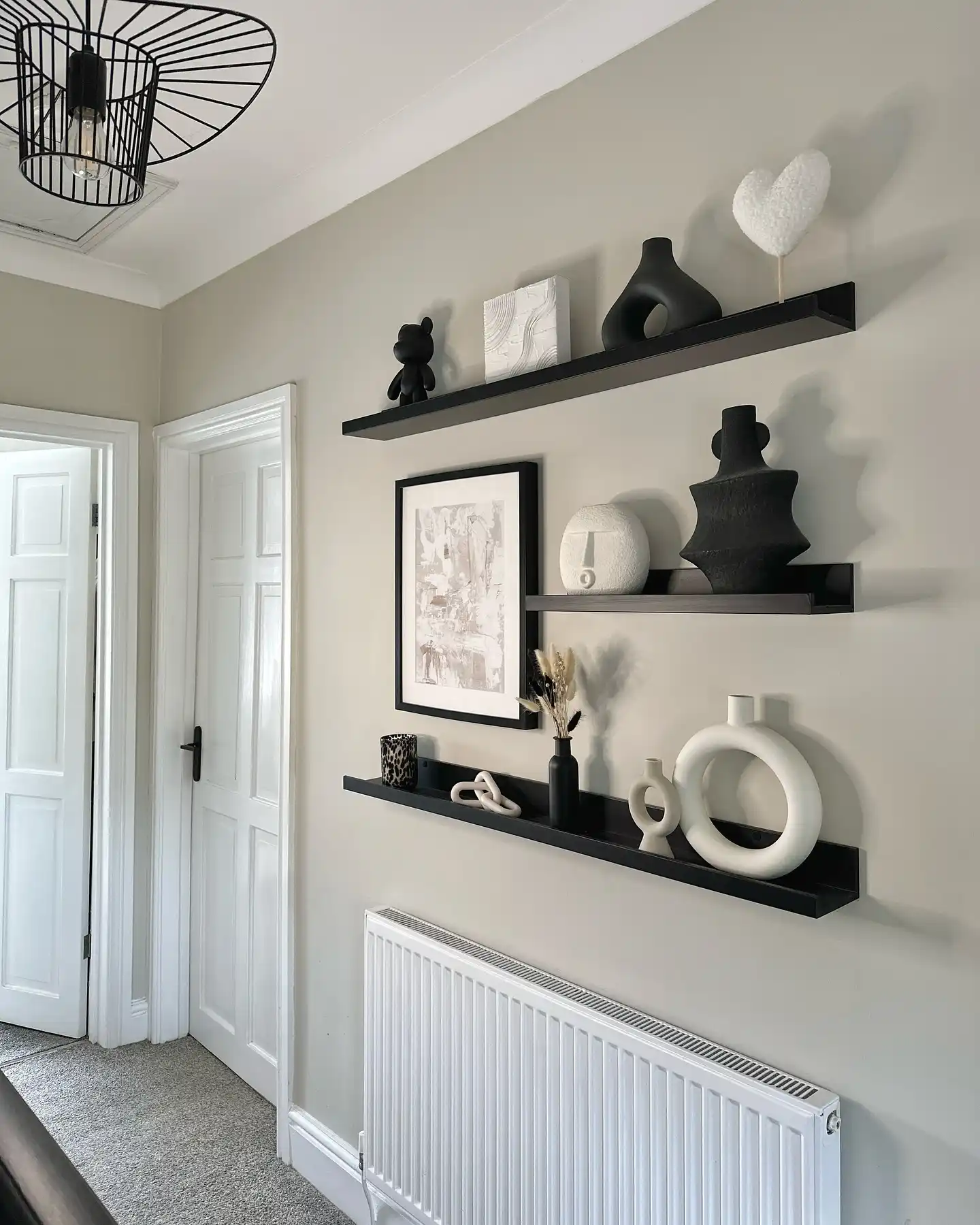 Hallway wall with black floating shelves styled with framed art, sculptural decor, and black and white accents