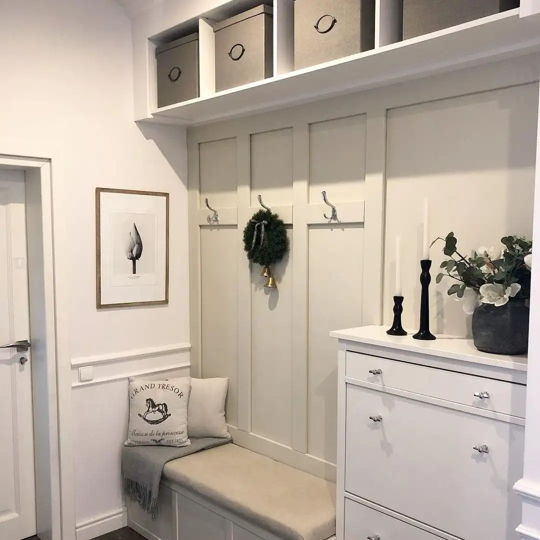 Compact mudroom drop zone with cushioned bench, wall hooks, upper storage cubbies, drawers, and soft neutral cabinetry.
