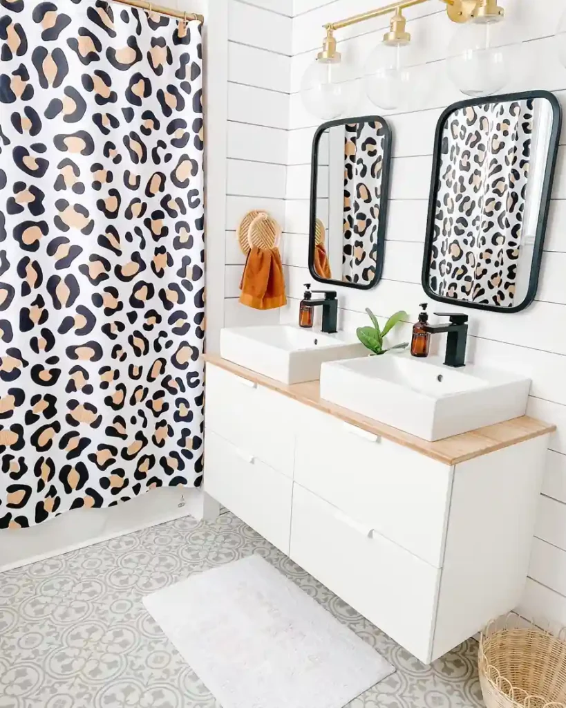 White double vanity bathroom with a leopard-print shower curtain, black mirrors and faucets, and a burnt-orange towel.