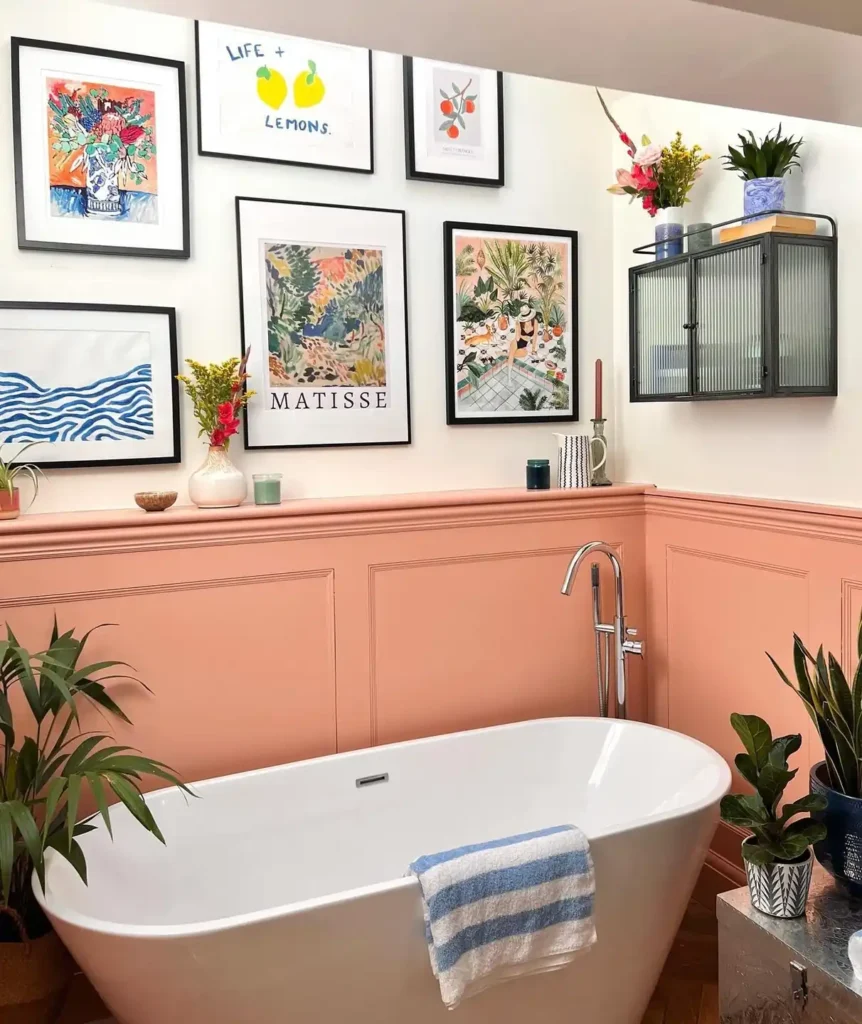 Colorful bathroom gallery wall with botanical prints, abstract art, and simple black frames above coral wall paneling.
