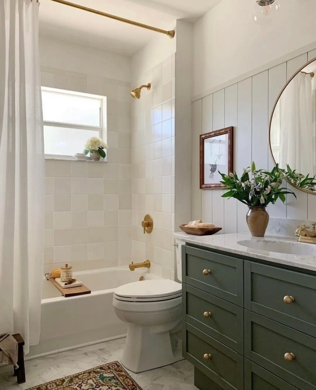 Small bathroom with a ceiling-high white shower curtain, dark green vanity, round mirror, and brass fixtures.