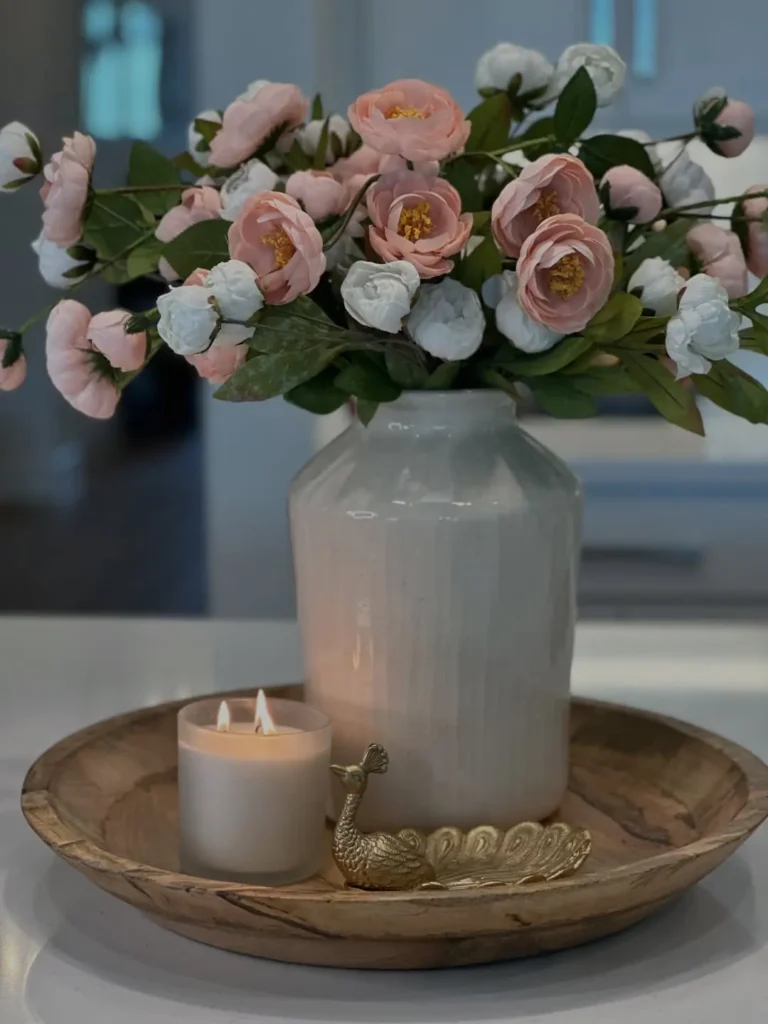 Rustic wooden tray with a white vase of pink flowers, glowing candle and small gold bird dish.