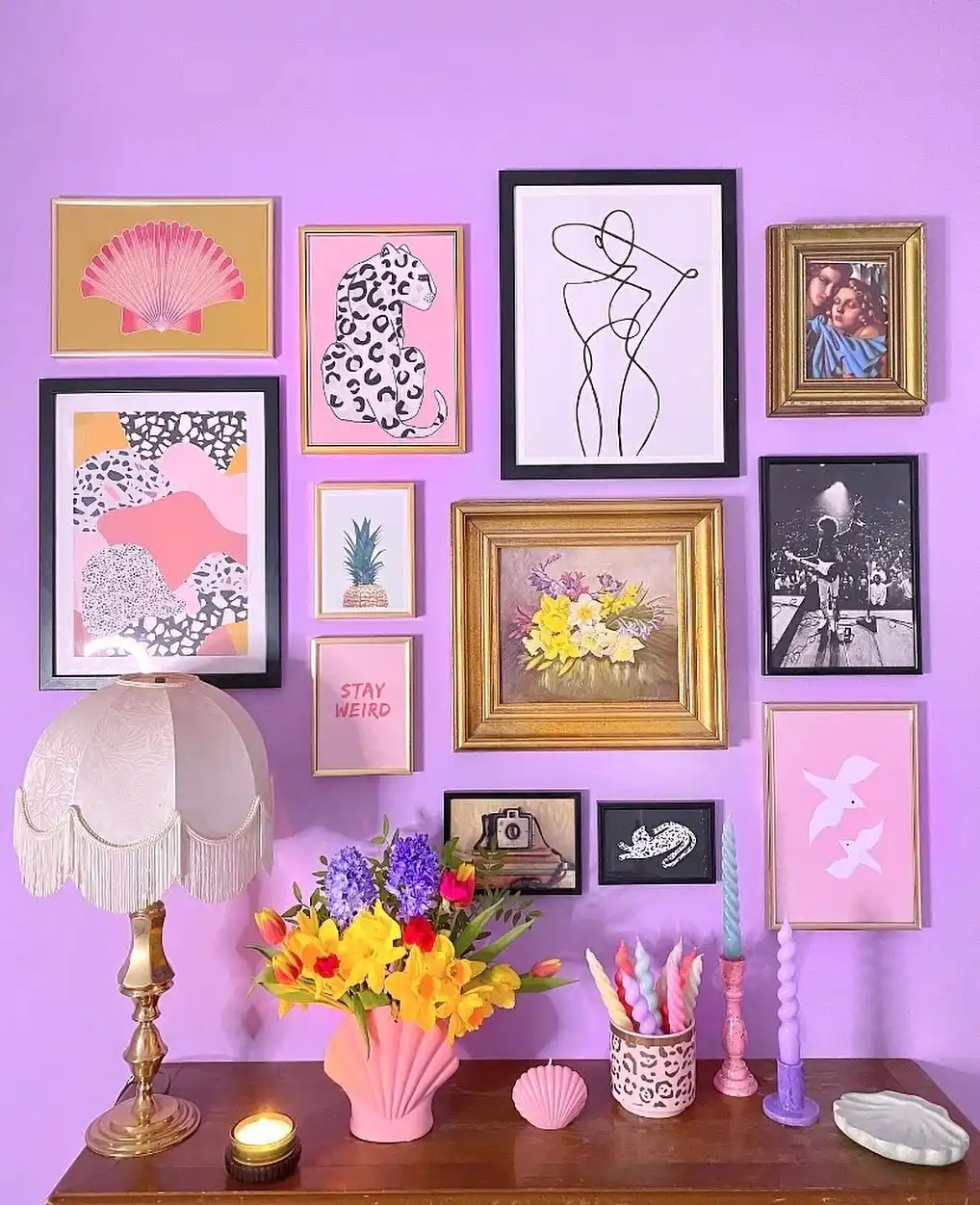 Colorful lavender hallway with eclectic gallery wall, fringed lamp, flowers, candles, and mixed picture frames
