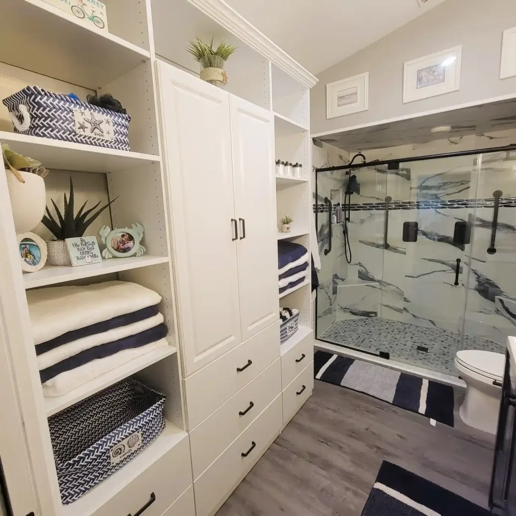 Built in bathroom storage with folded towels on open shelves, woven baskets, drawers, and a tall closed cabinet.