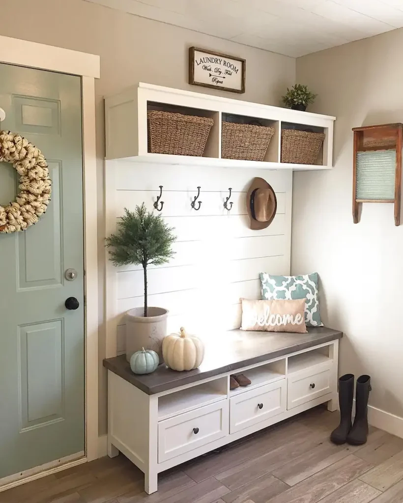 White entryway bench with drawers, wall hooks, woven storage baskets, and space for backpacks and shoes.
