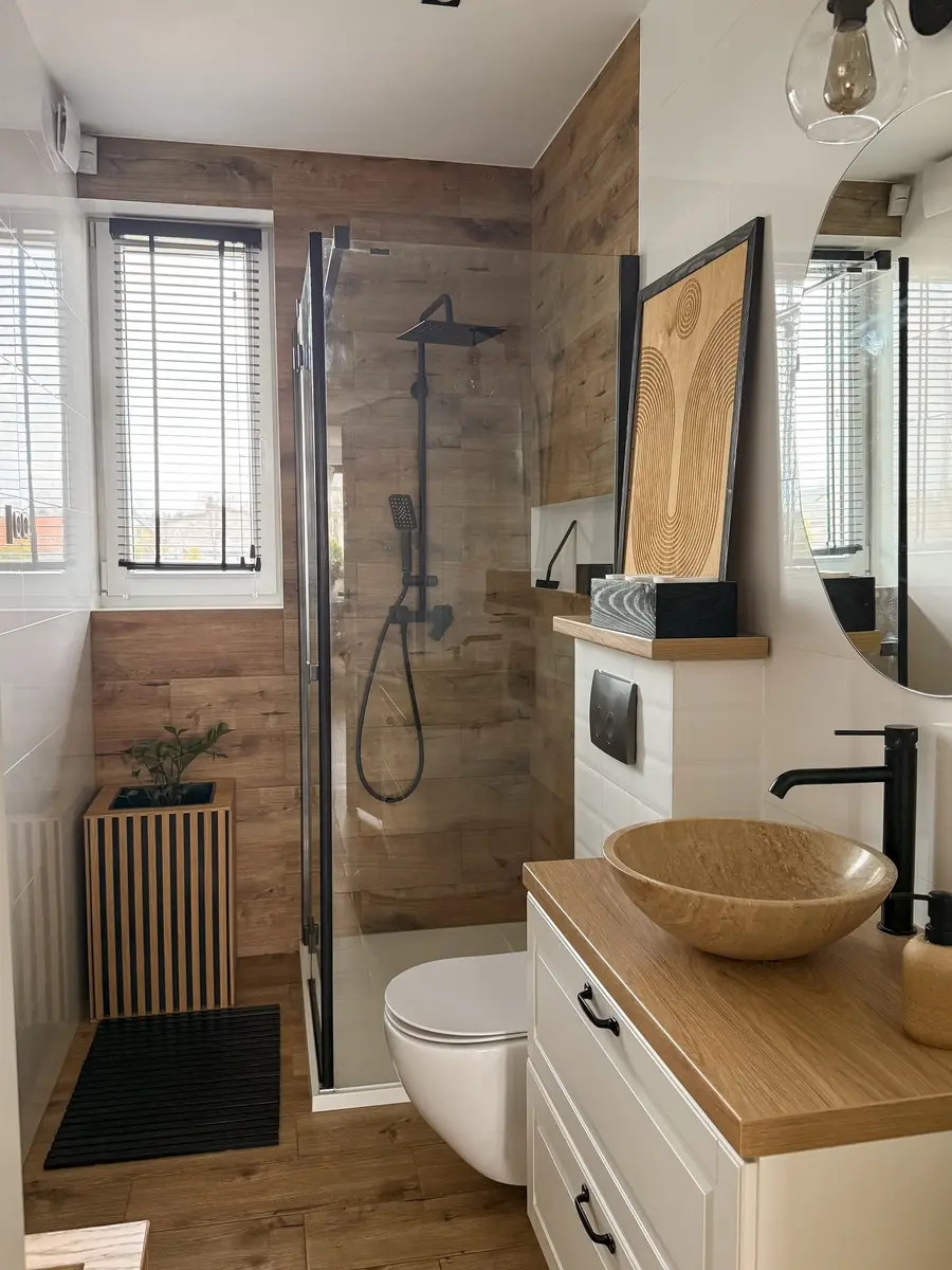 Narrow modern bathroom with wood-look shower tiles, clear glass, a bowl sink, and matte black fixtures.