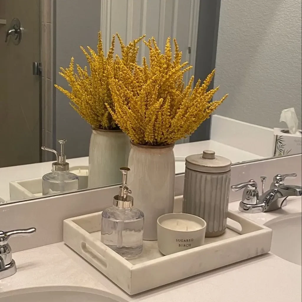 White rectangular bathroom tray with golden flowers, clear soap dispenser, candle and grey lidded jar.