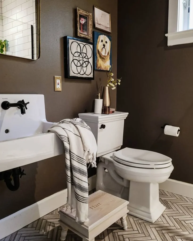 Small bathroom gallery wall with a playful dog portrait, abstract black line art, and small framed paintings on a dark wall.