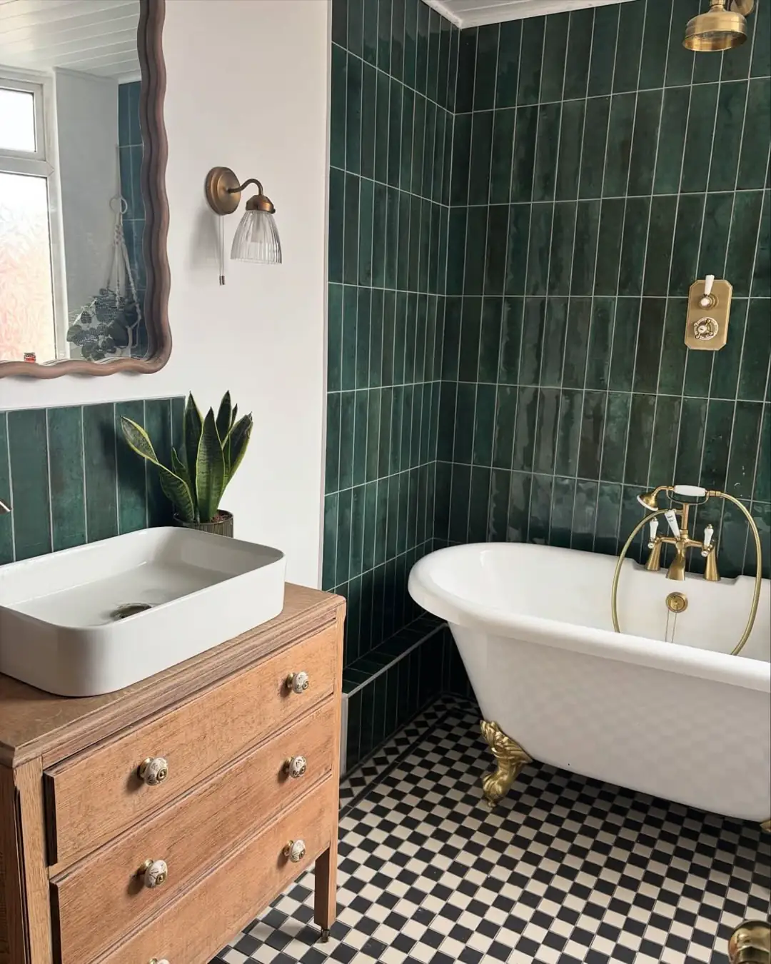 Small dark green powder room with pedestal sink, white cabinet, gold-framed gallery wall and wood flooring