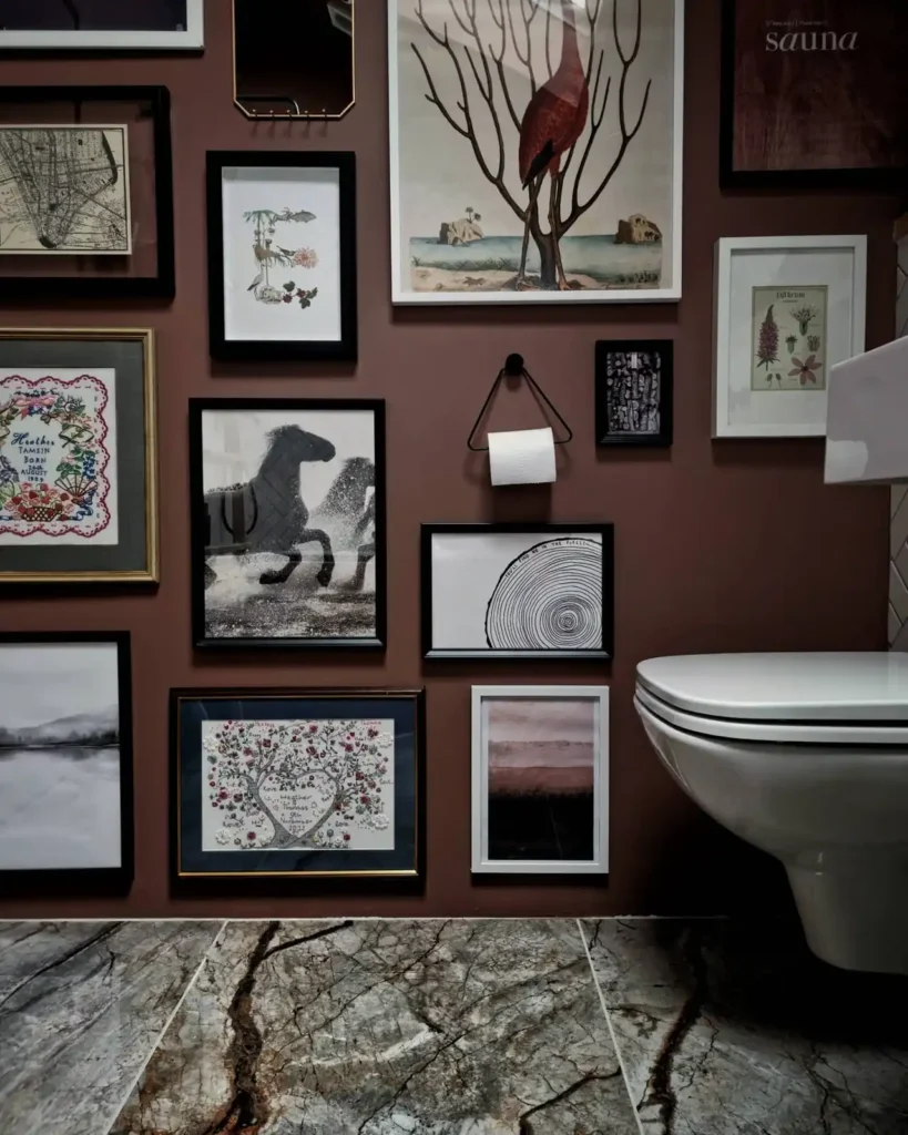 Floor to ceiling bathroom gallery wall with bird art, botanical prints, photography, embroidery, and mixed frames on a brown wall.