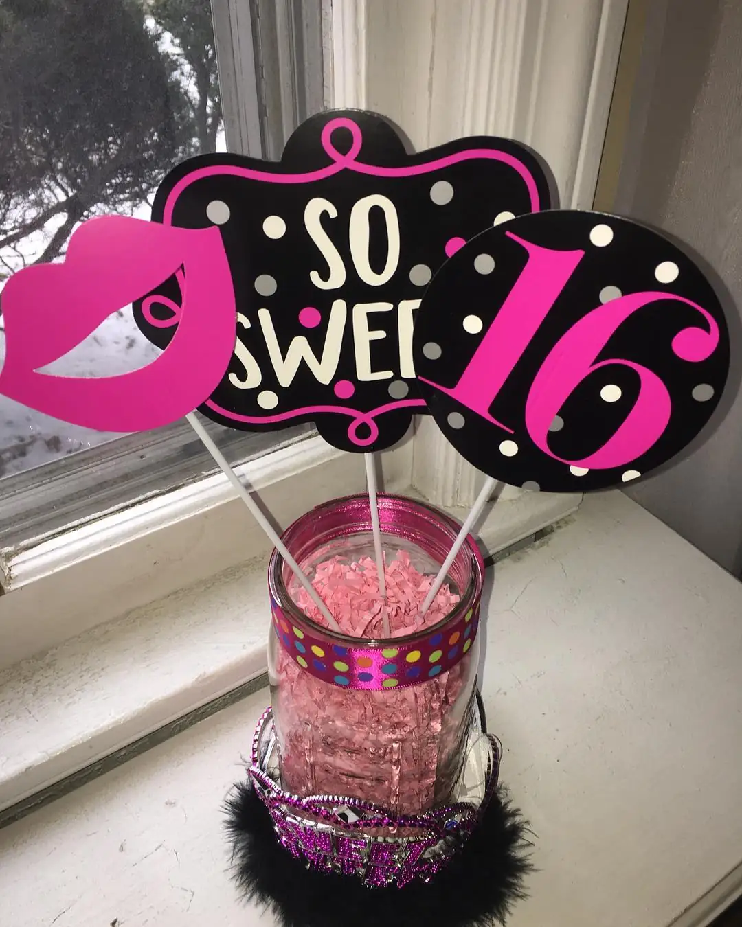 Pink black and white Sweet 16 party signs arranged in a decorated mason jar with paper filler