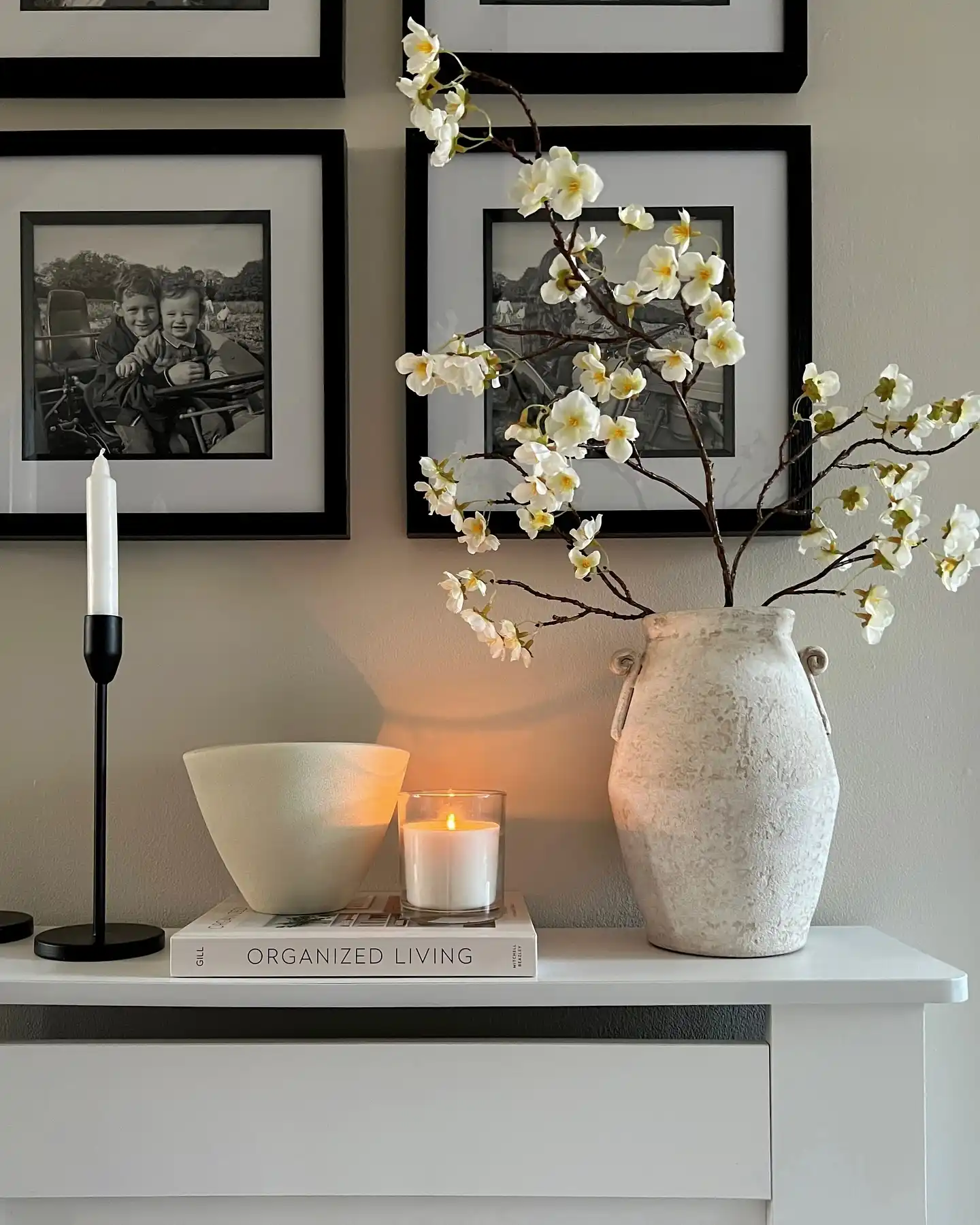 Hallway console styled with tall blossom branches, black framed family photo gallery, candles, and ceramic decor