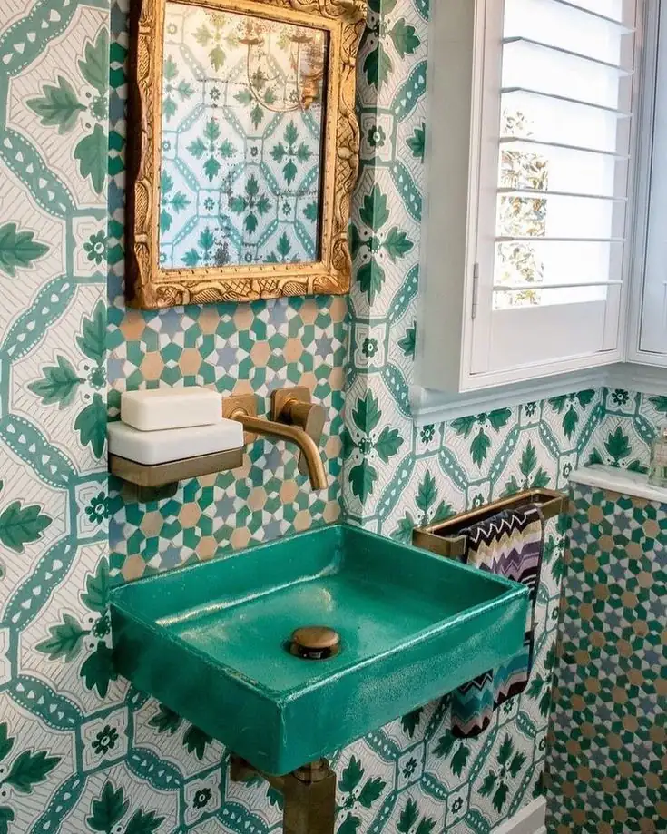 Modern dark green tiled bathroom with coral wall-mounted sink, round brass mirror, glass shower and brass accents