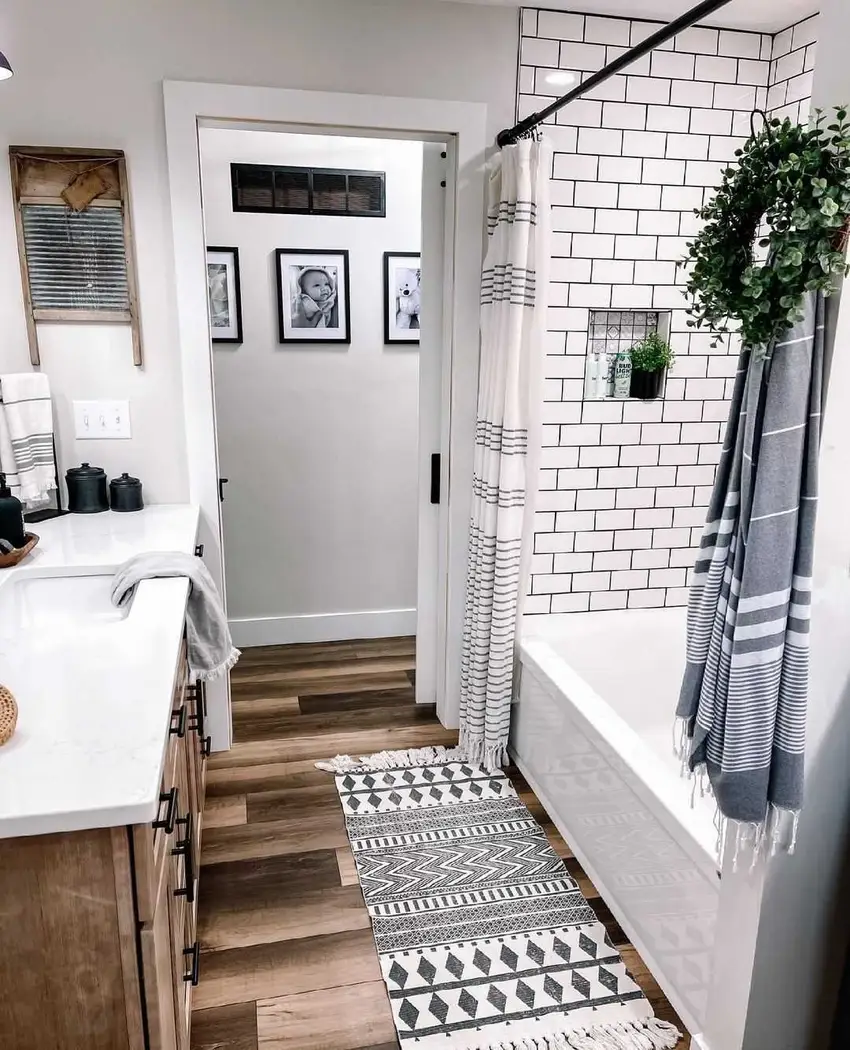 Modern farmhouse bathroom with white subway tile, warm wood vanity, black fixtures, striped towels, and wood-look flooring