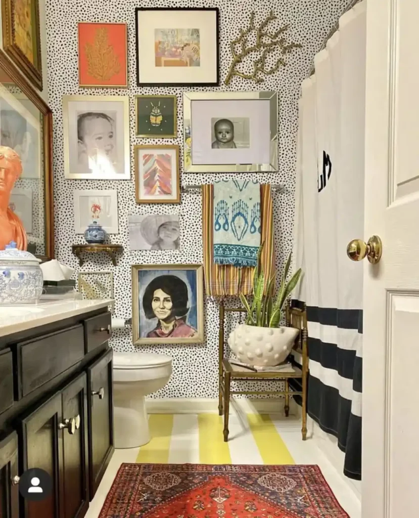 Eclectic bathroom gallery wall mixing personal black and white photos, colorful artwork, and portraits over dotted wallpaper.