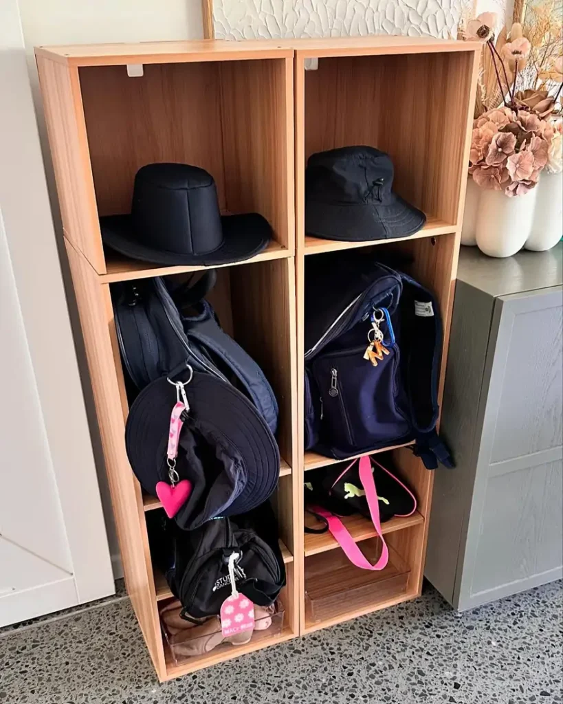 Narrow wooden cubby unit storing backpacks, hats, smaller bags, and school accessories in vertical compartments.