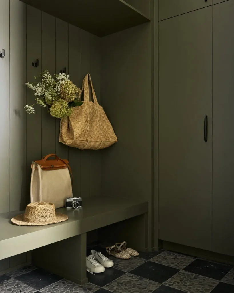 Deep green drop zone with tall cabinets, an open bench, wall hooks, and shoe storage below.