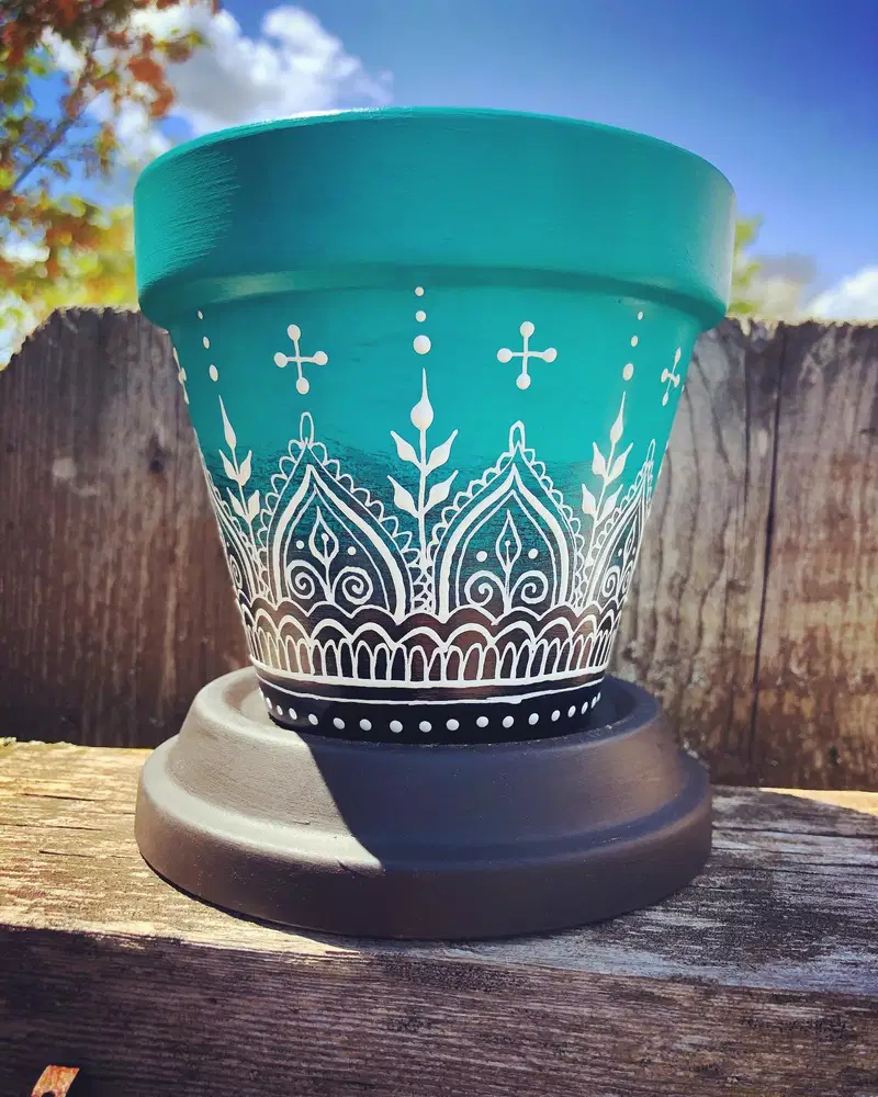 Turquoise flower pot decorated with detailed white folk art arches, leaves, curls, and dots
