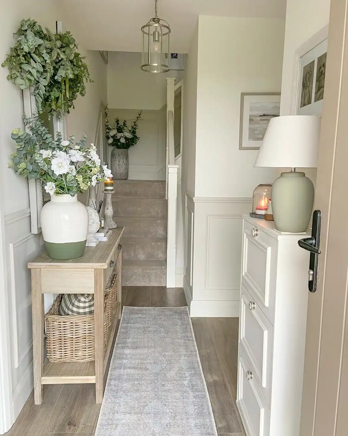 Narrow hallway with slim wood console, white storage cabinet, woven baskets, runner rug, and soft sage accents