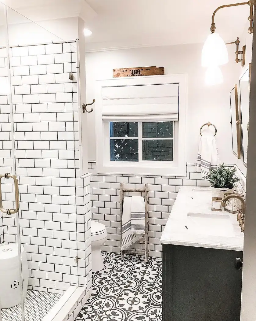 Black-and-white modern farmhouse bathroom with patterned floor tile, white subway tile, dark vanity, ladder towel rack, and brass fixtures