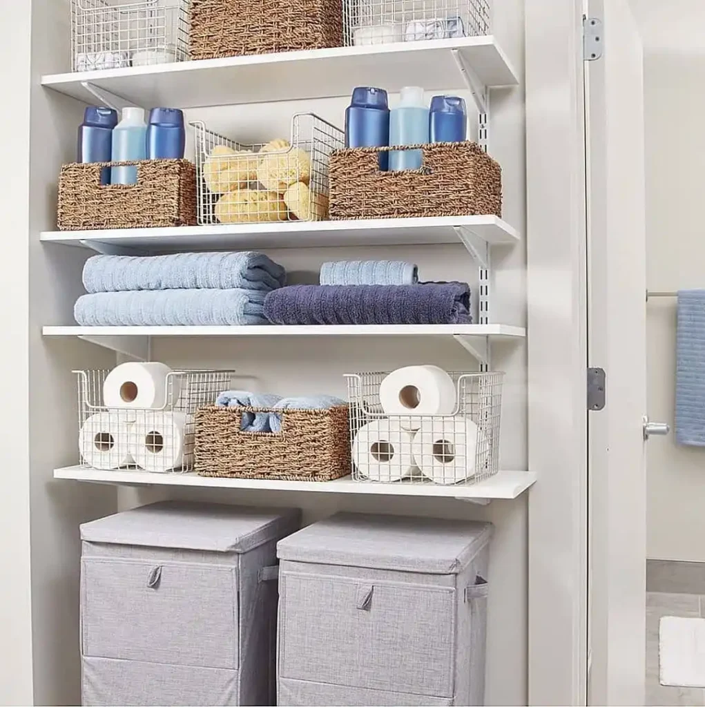 Open bathroom closet with folded towels, woven baskets, wire baskets, toilet paper storage, and large fabric hampers.