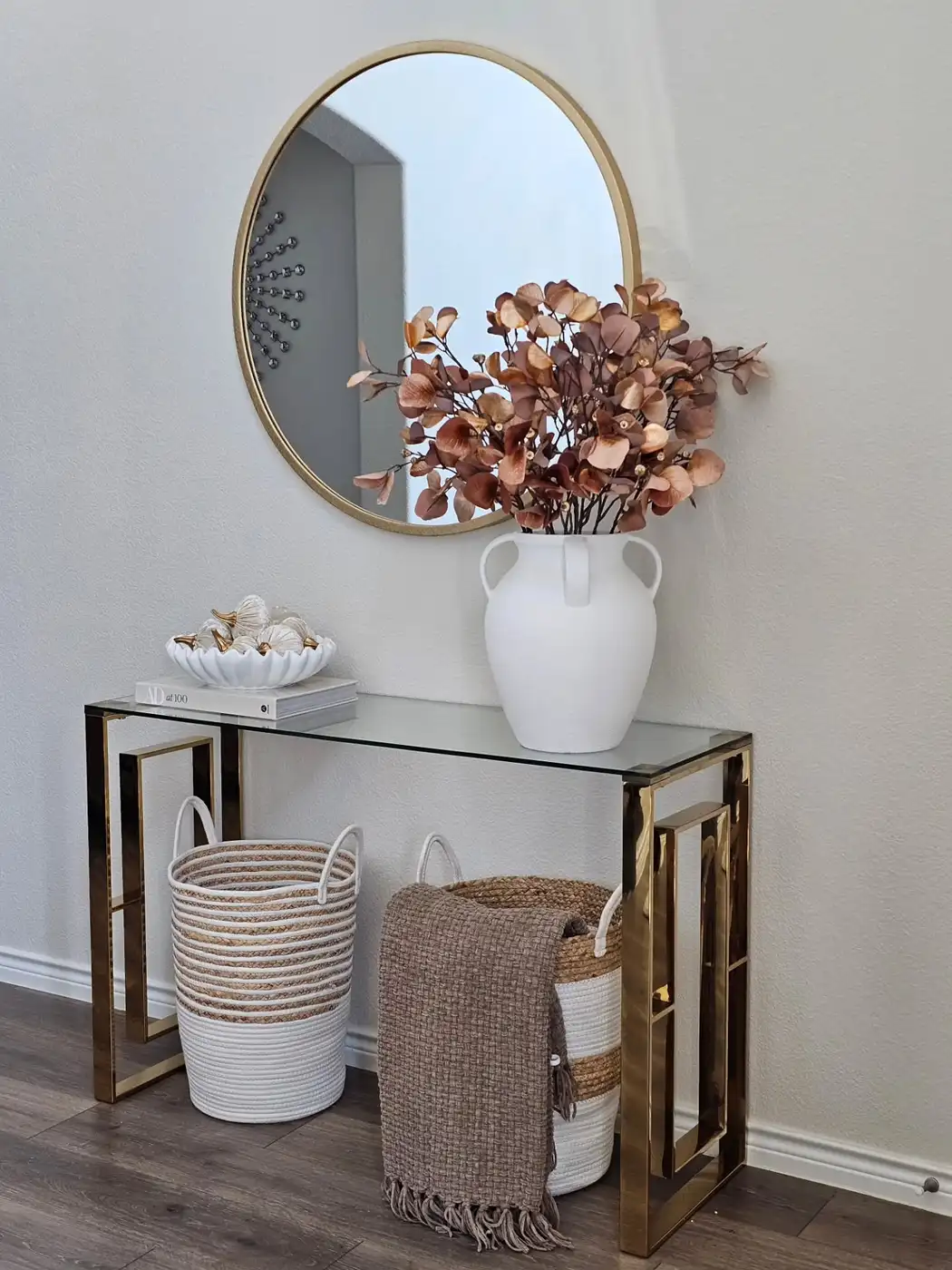 Narrow glass console table with two woven baskets underneath and round wall mirror