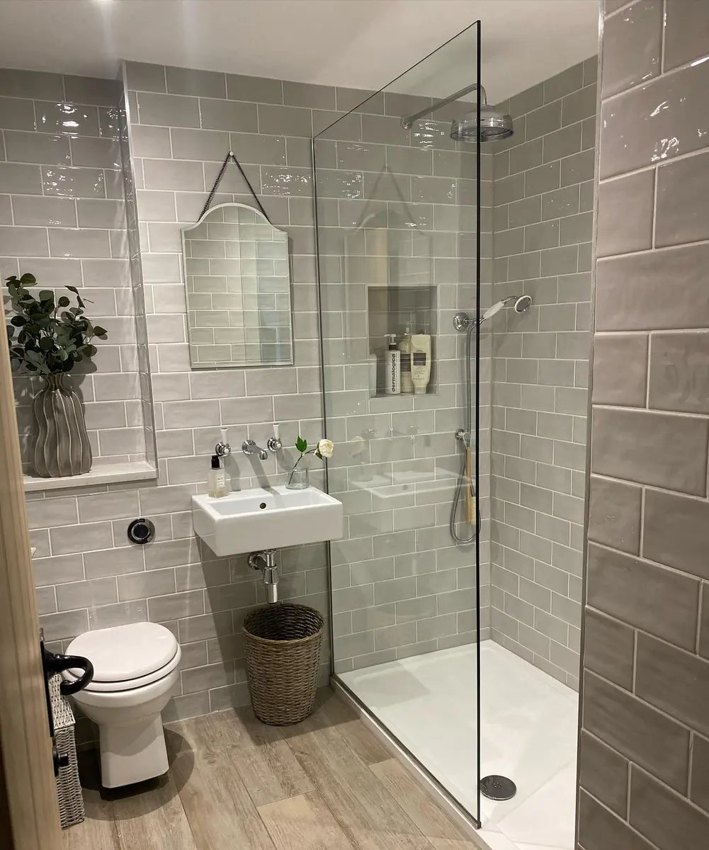 Compact gray-tiled bathroom with a wall-mounted sink, recessed storage niches, and a frameless glass shower.