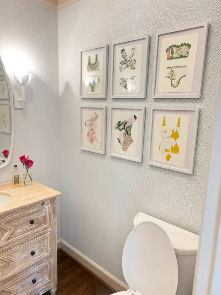 Neat bathroom gallery wall with six matching white frames arranged in a grid over subtle patterned wallpaper.