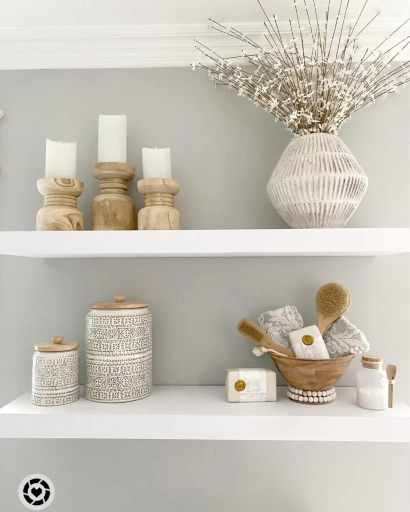 Neutral bathroom shelves styled with wooden candleholders, textured vase, patterned storage jars, soaps, and bath brushes.