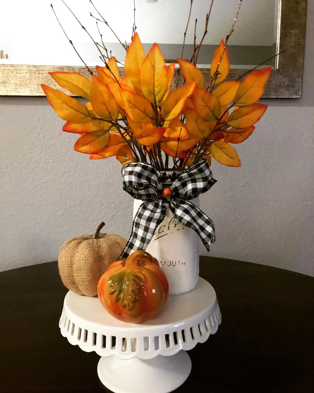 White painted mason jar filled with orange leaves and twigs, finished with a black and white gingham bow
