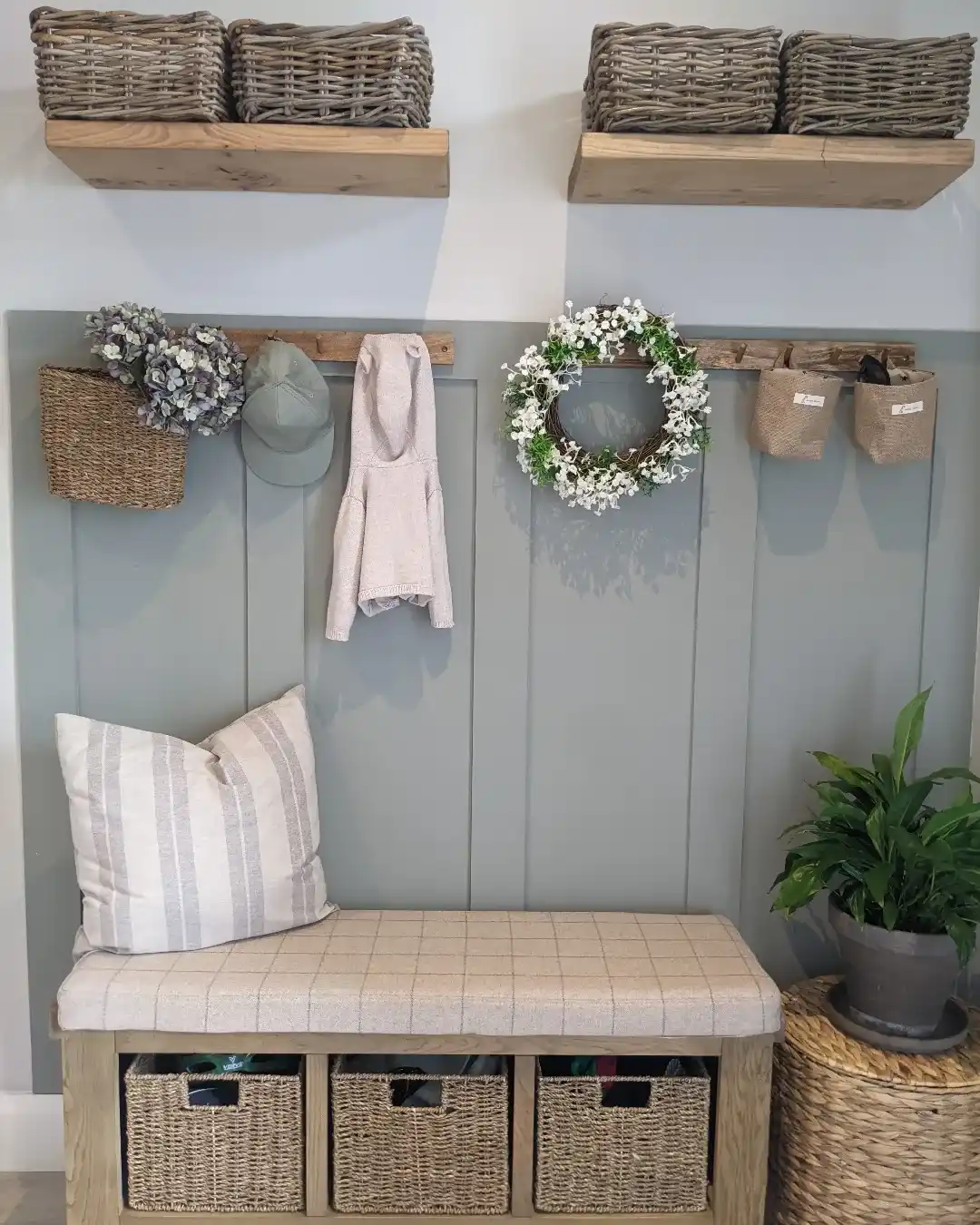 Hallway storage bench with woven baskets, wall hooks, open wood shelves, cushions, and muted green paneling