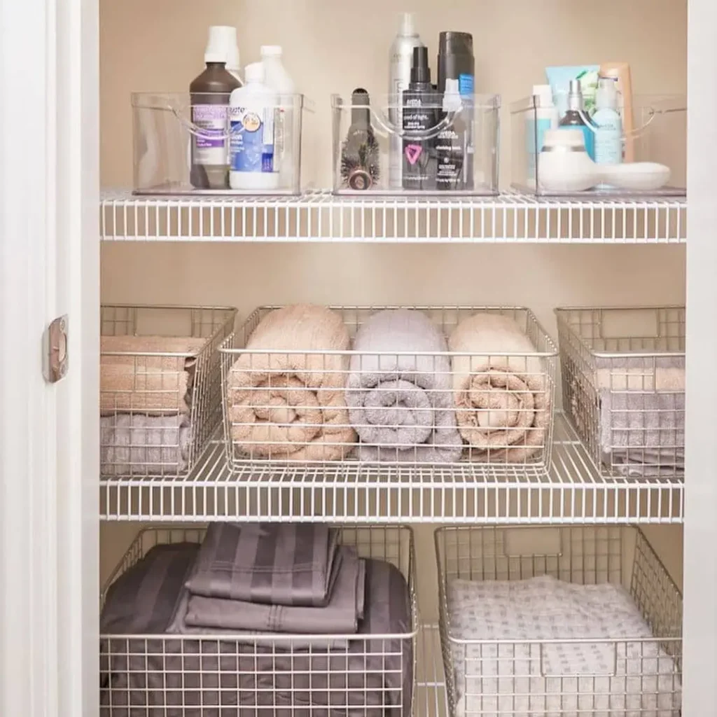 Bathroom closet with clear bins for toiletries, wire baskets for rolled towels, and larger baskets for folded linens.