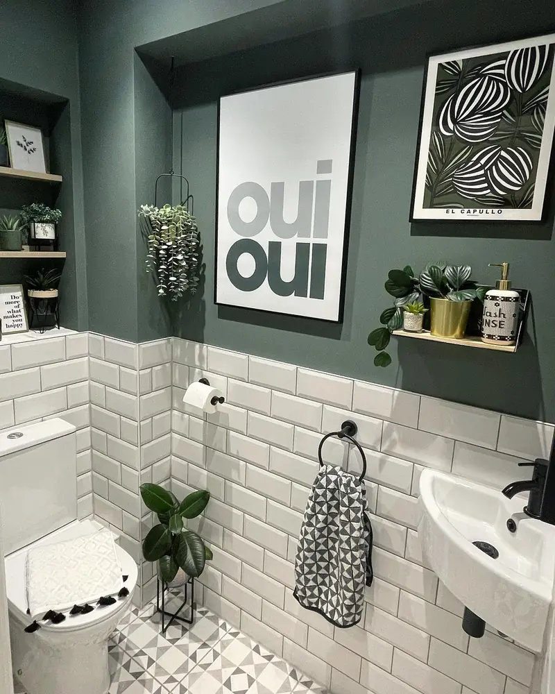 Dark green small bathroom with white subway tiles, a compact sink, oversized wall art, shelves, and plants.