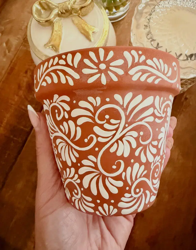 Terracotta flower pot decorated with creamy white swirling folk florals, leaves, and dots