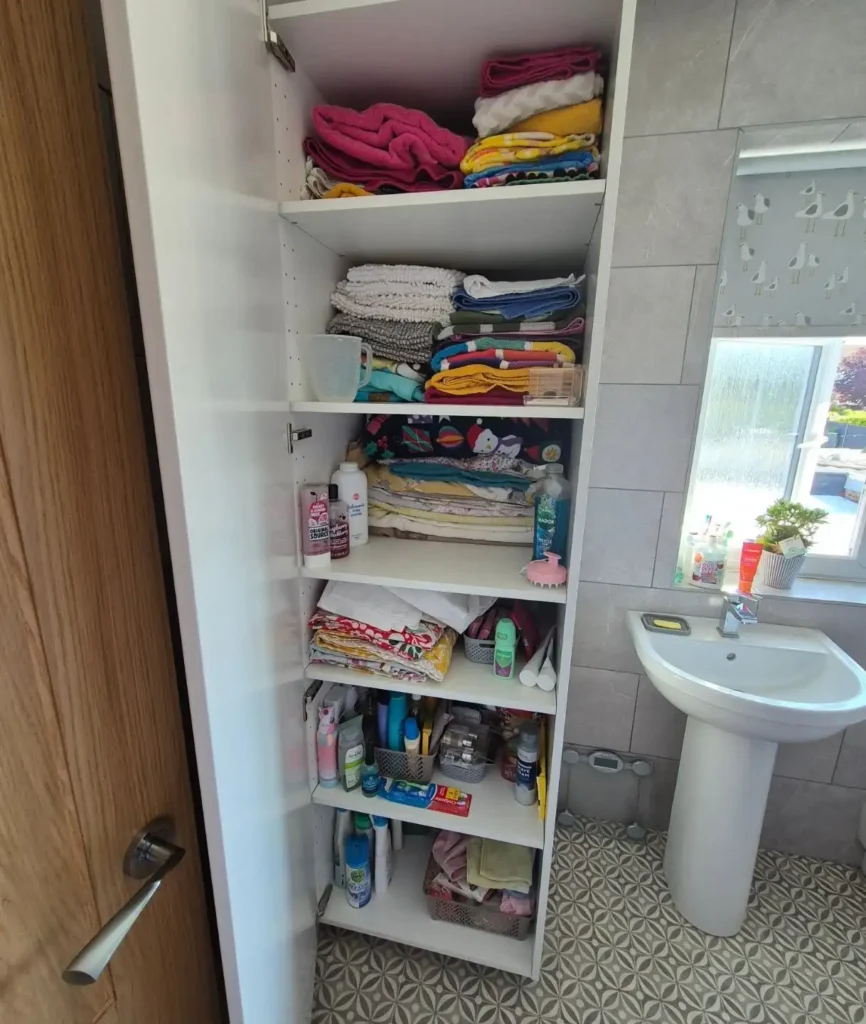 Tall narrow bathroom closet with shelves organized for folded towels, washcloths, toiletries, and backup bathroom supplies.