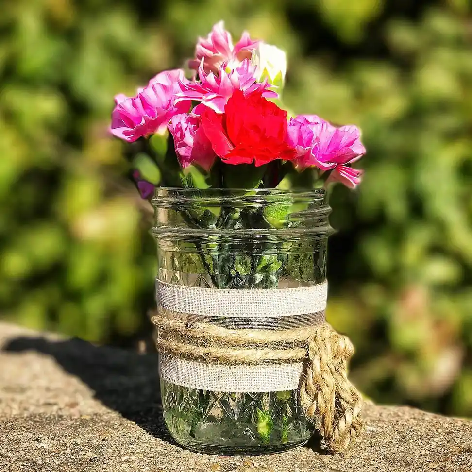 Bright pink flowers in a clear mason jar wrapped with neutral ribbon and chunky rustic rope