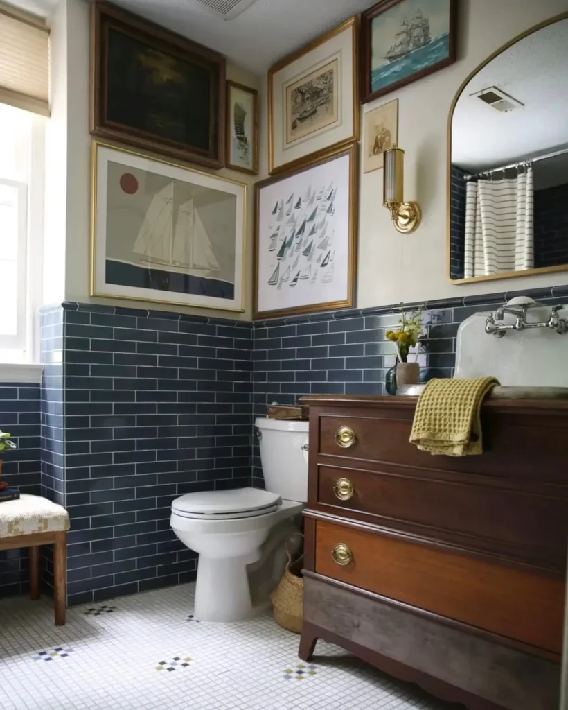 Coastal bathroom gallery wall with sailboat prints, ship paintings, and maritime artwork above dark blue subway tile.