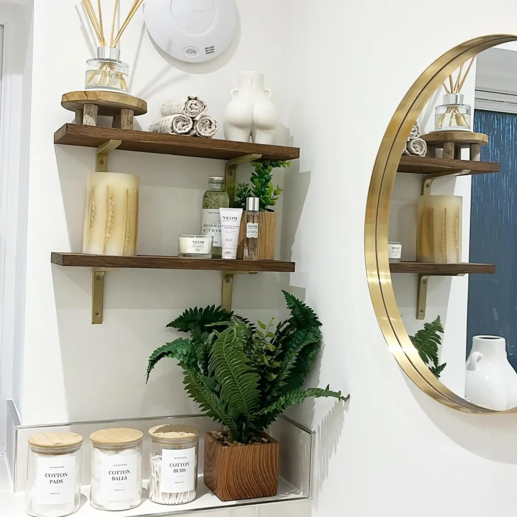 Warm wood bathroom shelves with brass brackets, rolled washcloths, diffuser, skincare products, candle, and greenery.